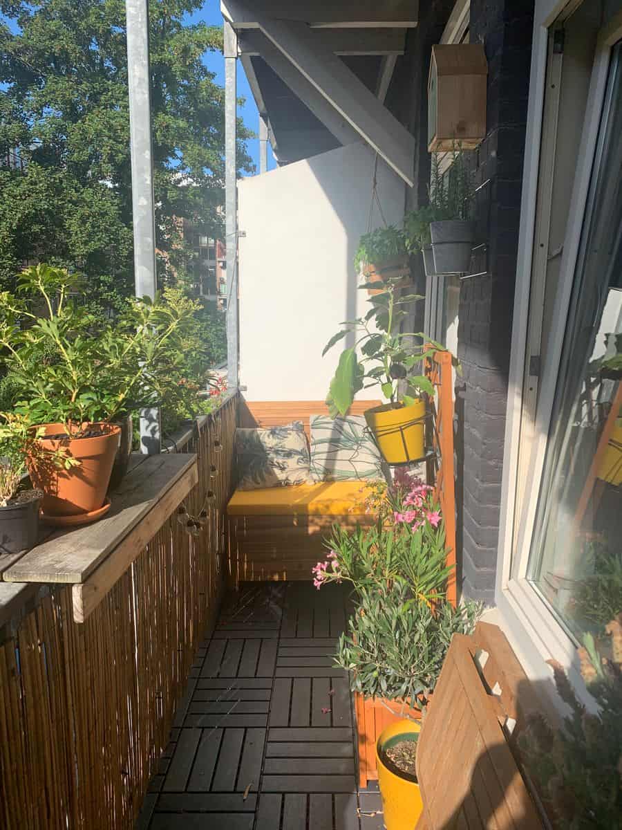 Klein balkon inrichten: 8 slimme en stijlvolle ideeën Weelderige balkontuin rondom een balkonbankje, met plantenbakken, bloempotten en een verticale balkontuin voor een groene en sfeervolle uitstraling.