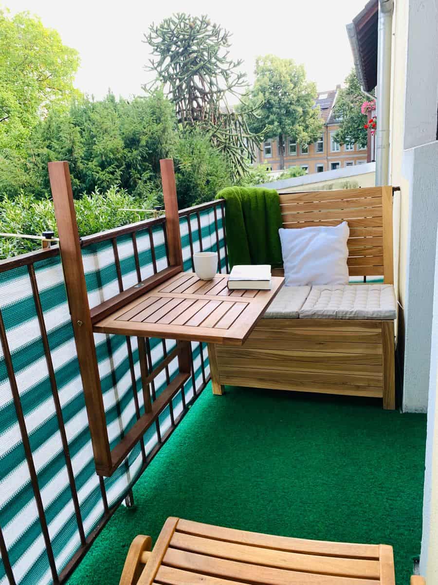 Klein balkon inrichten: 8 slimme en stijlvolle ideeën Balkonbank met opbergruimte van 100 cm breed, canvas kussens, en een inklapbaar balkontafeltje aan de reling op een klein en smal balkon.